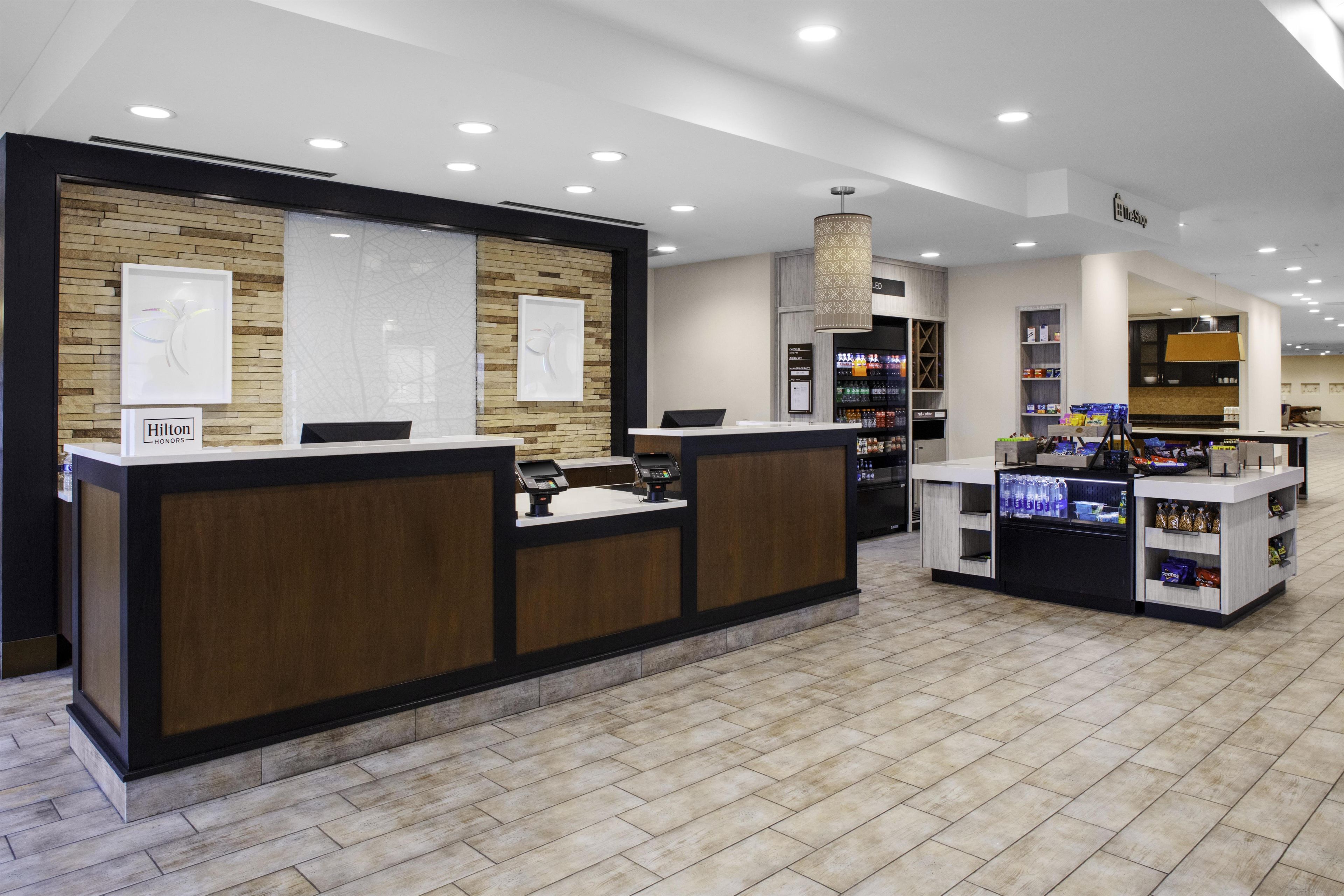 A hotel reception area with a wooden reception desk, a digital display, and a counter with snacks.