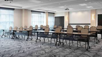A conference room with multiple tables and chairs, large windows, and a projector on the ceiling.
