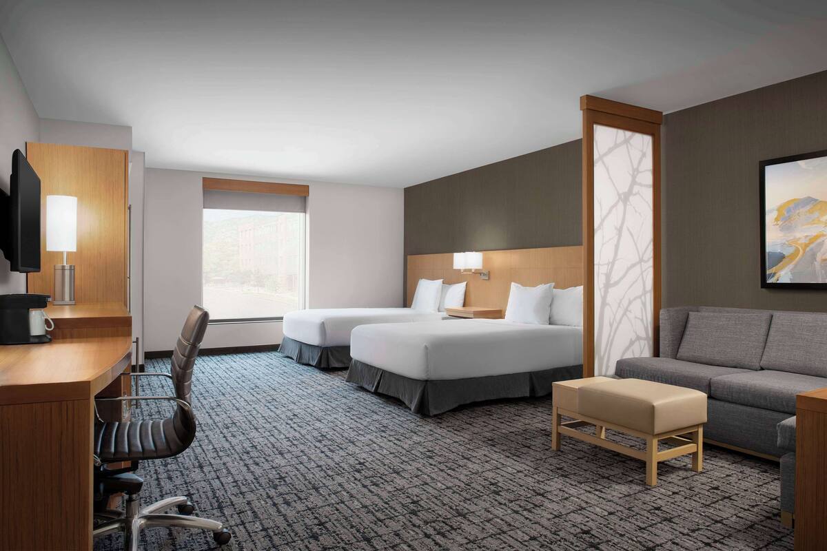 A hotel room with a desk, two beds, a sofa, and a TV.