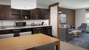 A modern kitchen with dark wood cabinets, a microwave, and a coffee maker. There is a dining table with chairs and a sofa in the living area.