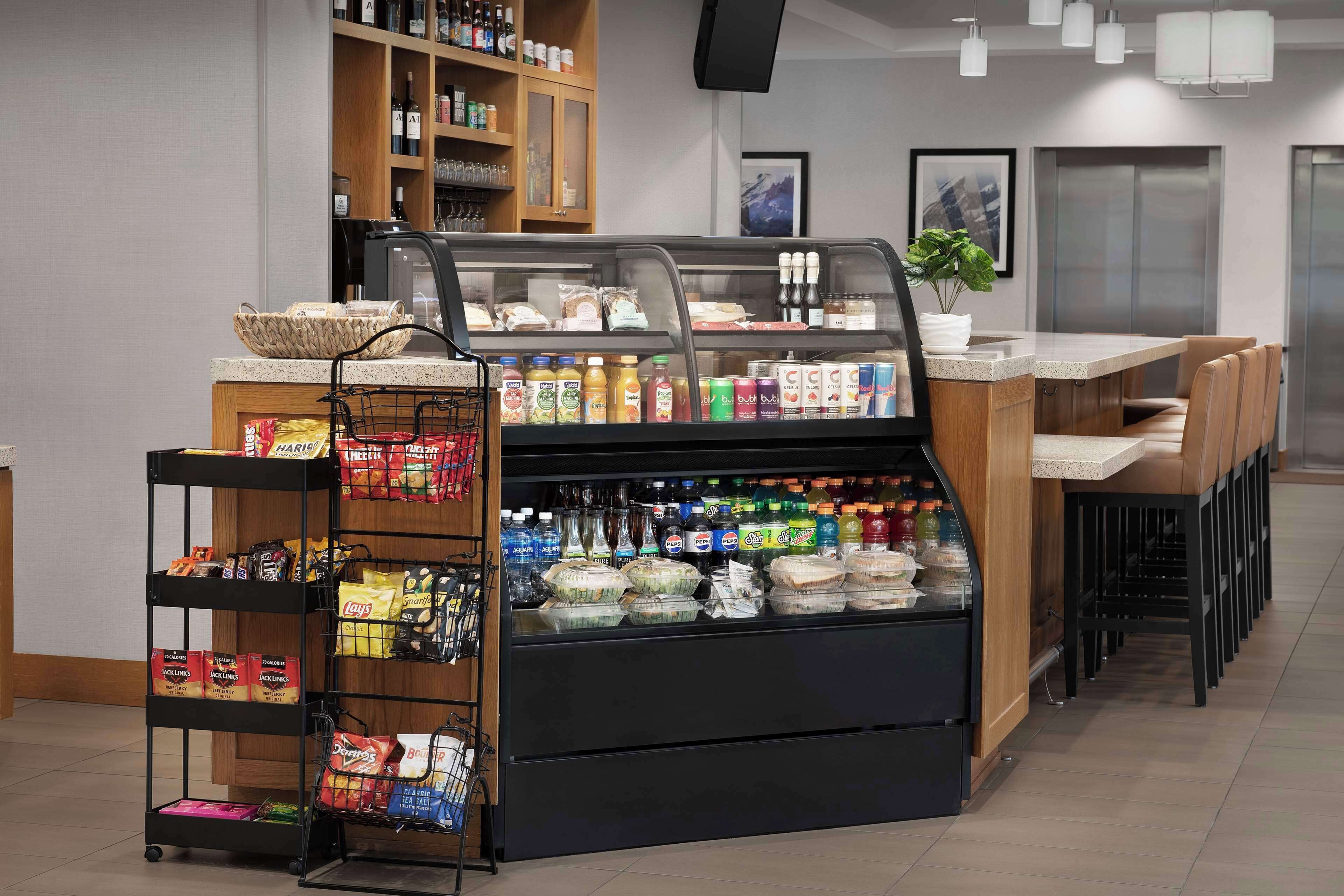 Un espace de libre-service proposant une variété de boissons et d’en-cas, une machine à café et un coin salon avec des chaises et une table.