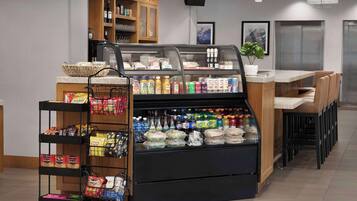 Un espace de libre-service proposant une variété de boissons et d’en-cas, une machine à café et un coin salon avec des chaises et une table.