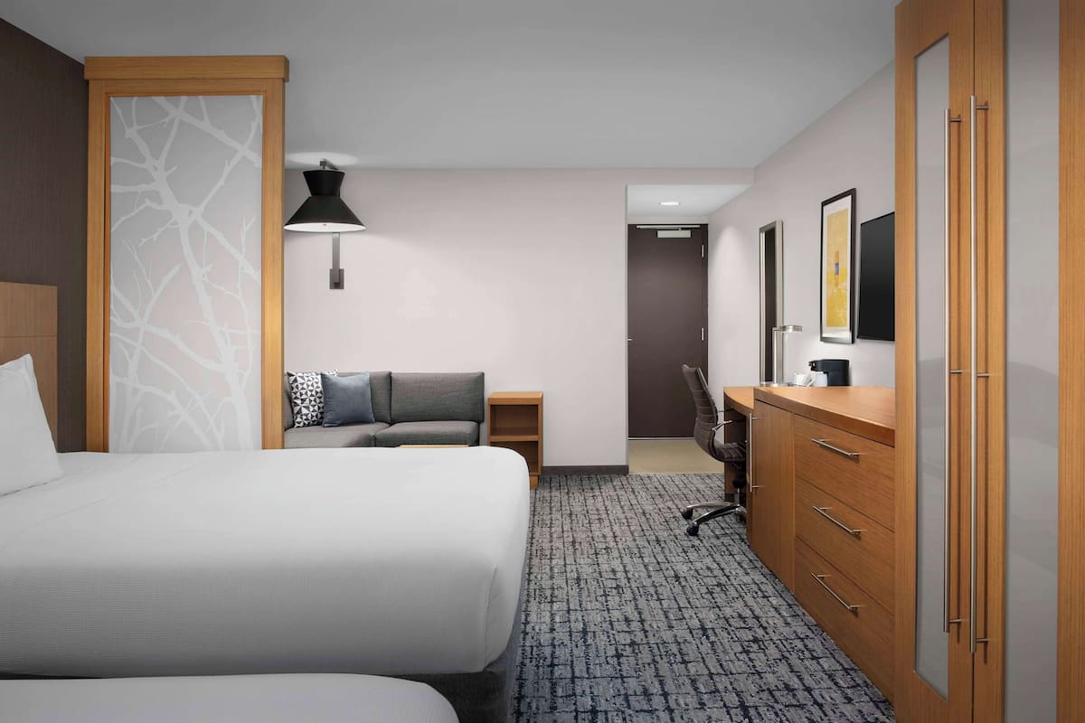 A hotel room with a large bed, a desk, a chair, a wardrobe, and a wall-mounted lamp.