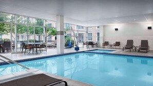 An indoor swimming pool with clear glass walls, a pool table, and lounge chairs.