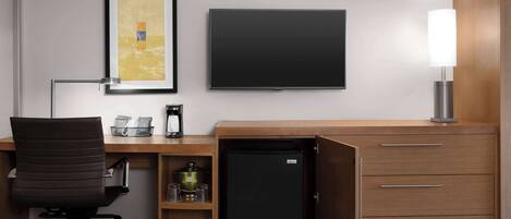 Et kompakt hotelværelse med skrivebord, stol, fladskærms-tv, minibar og lampe.
