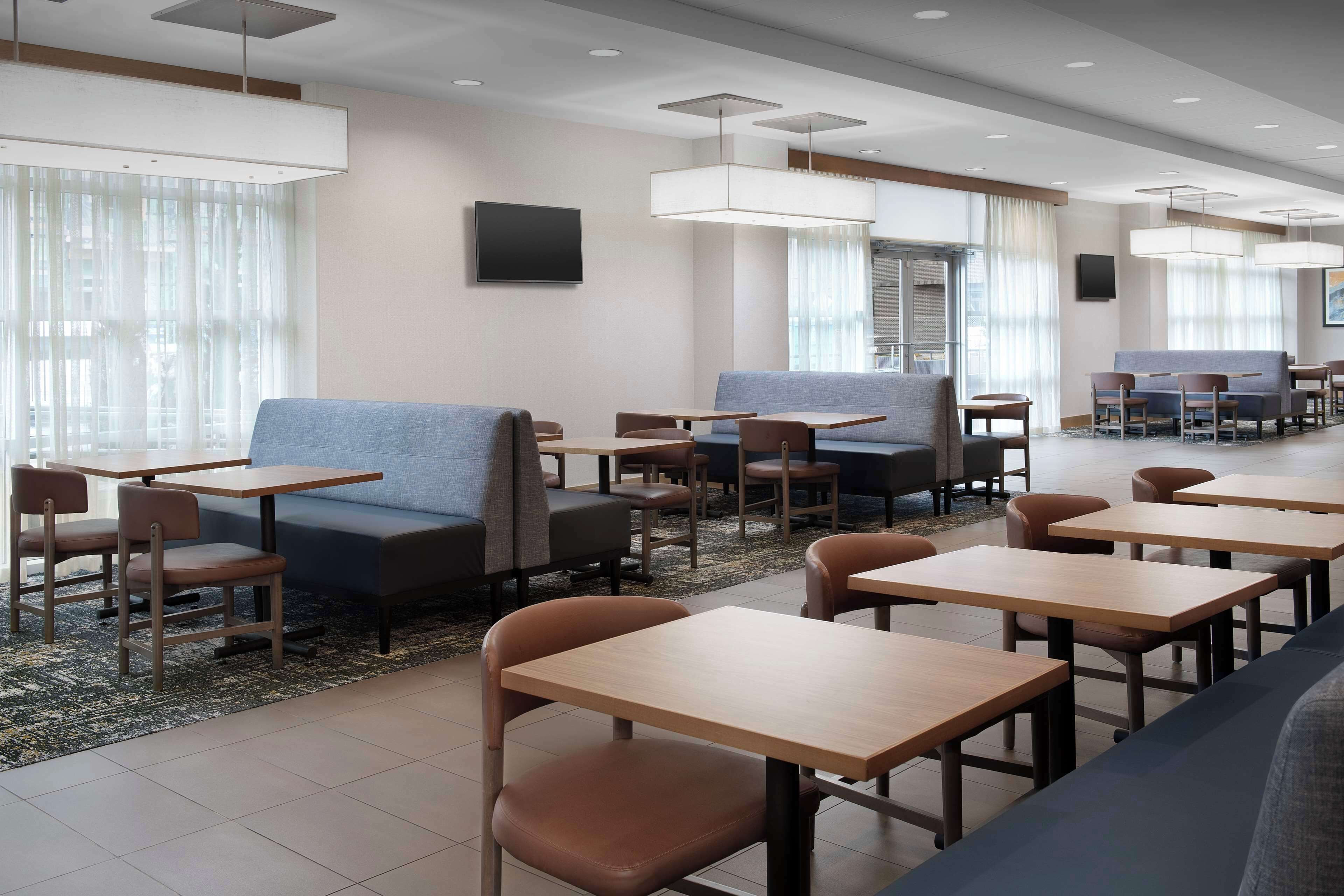 A modern hotel lobby with seating areas, tables, and a flat-screen TV on the wall.