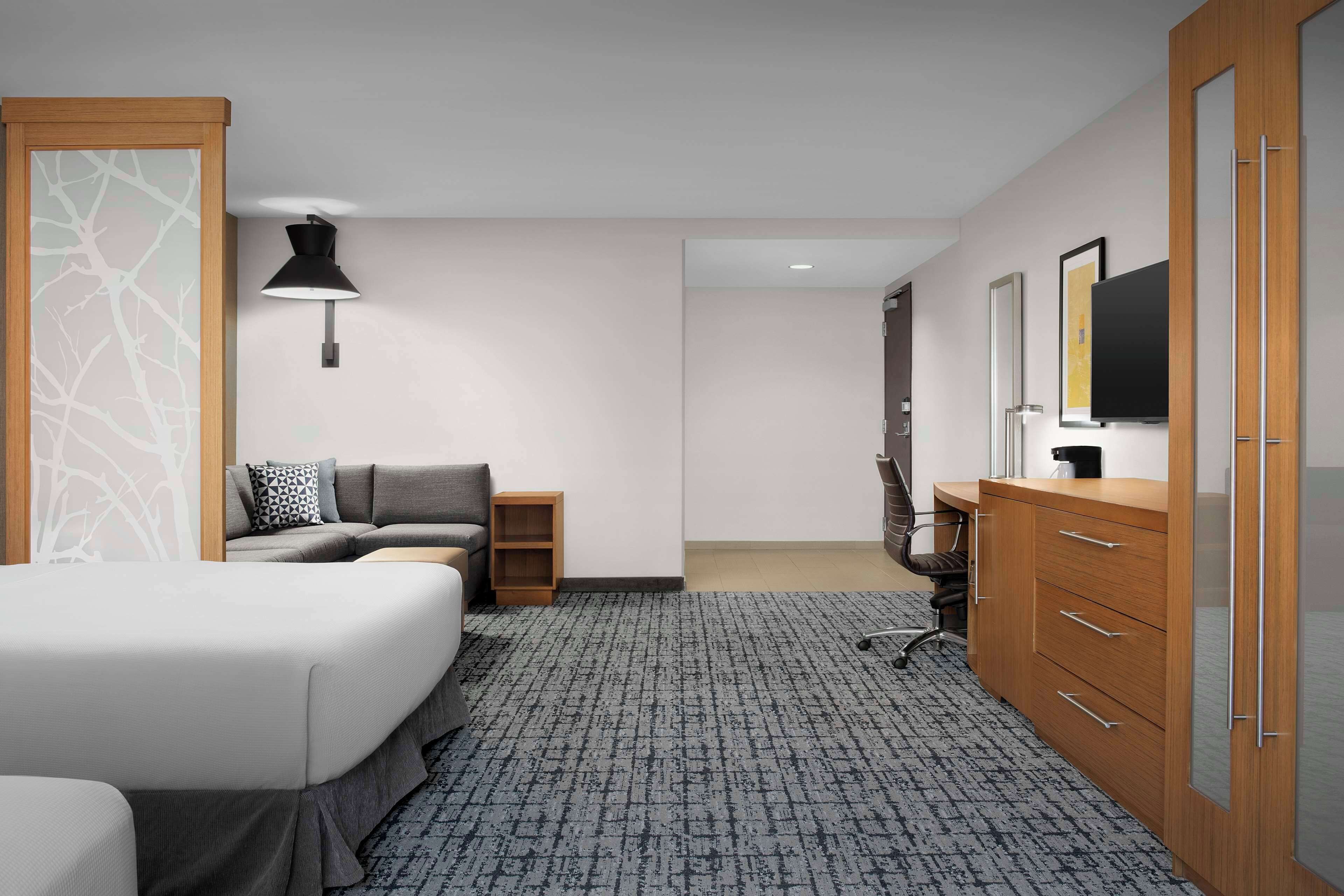 A hotel room with a bed, a desk, a chair, a lamp, a TV, and a wardrobe.