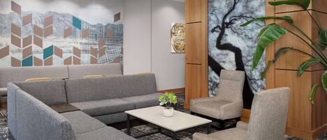 A modern lobby with a sectional sofa, a small table with a plant, and a large abstract painting on the wall.