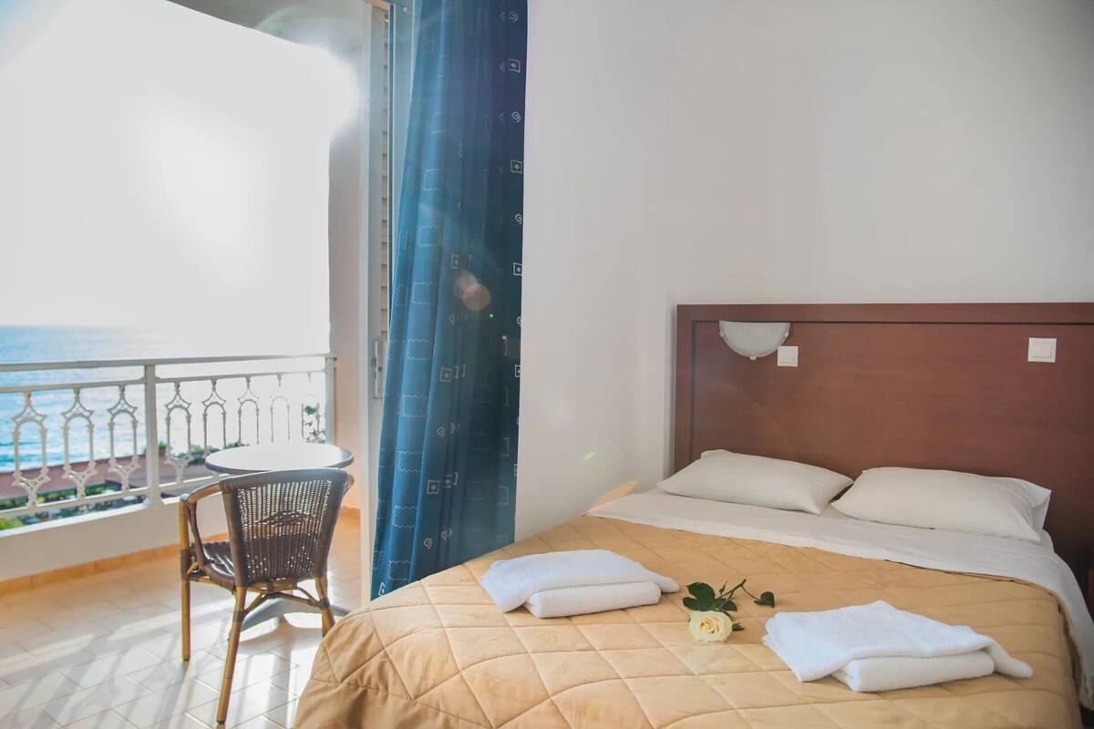 A hotel room with a bed, a chair, and a view of the sea.
