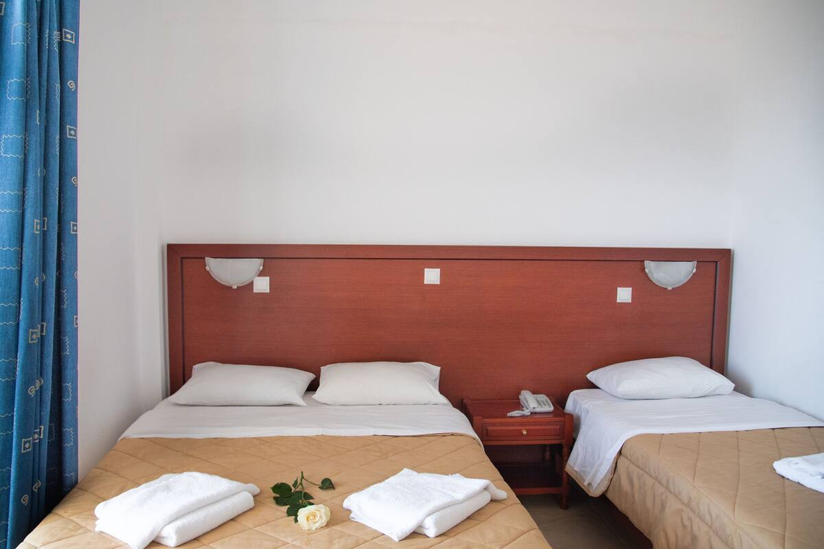 A hotel room with two beds, a wooden headboard, a bedside table with a phone, and a blue curtain.