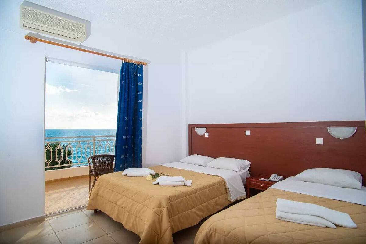 A hotel room with two beds, a balcony with a view of the sea, and an air conditioning unit.