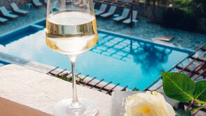 A glass of white wine on a balcony with a view of a pool and beach. - Poseidon Beach Hotel (Preveza)