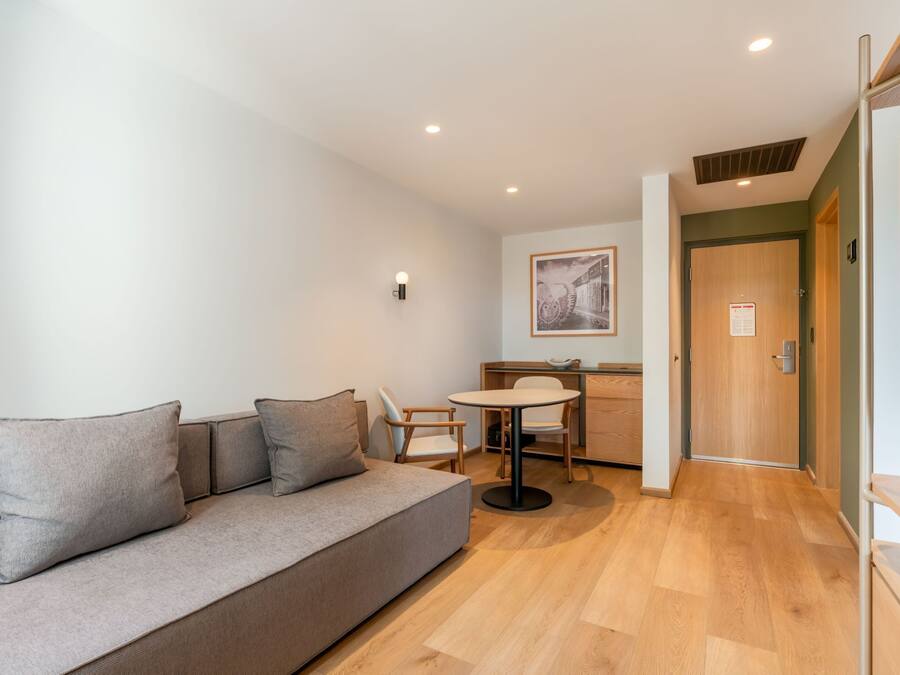 A modern living room with a sofa, a dining table, and a kitchen area in the background.