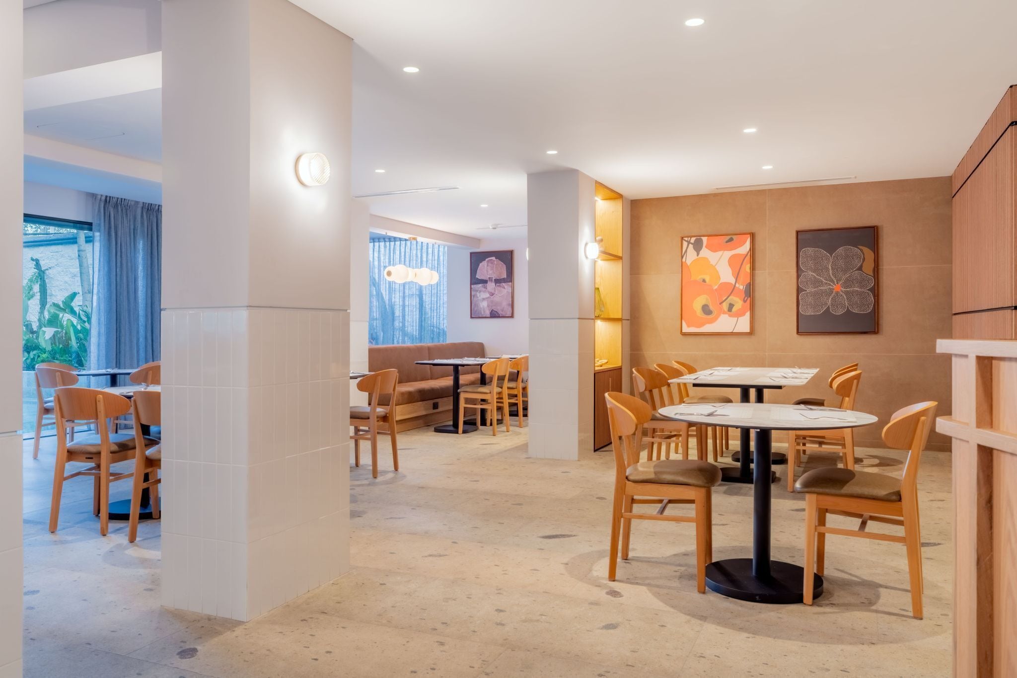 A modern interior with multiple seating areas, including round tables and booths, and a view of the outdoors through large windows.