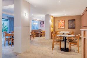 A modern interior with multiple seating areas, including round tables and booths, and a view of the outdoors through large windows. - Hilton Garden Inn Tijuana Airport (Tijuana)