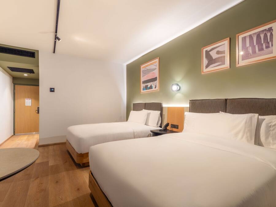 Une chambre d’hôtel avec deux lits, un bureau et une lampe fixée au mur.