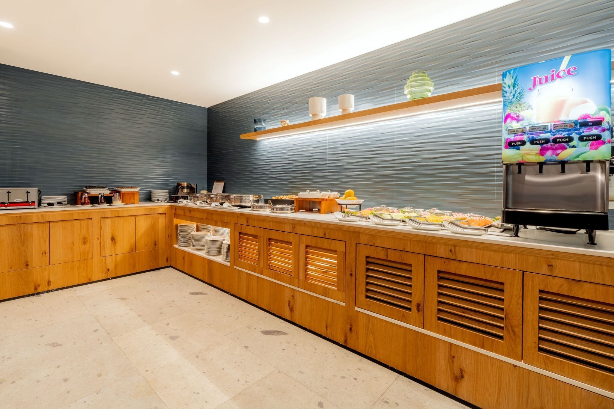 A modern kitchen area with a juice dispenser, buffet setup, and wooden cabinetry.