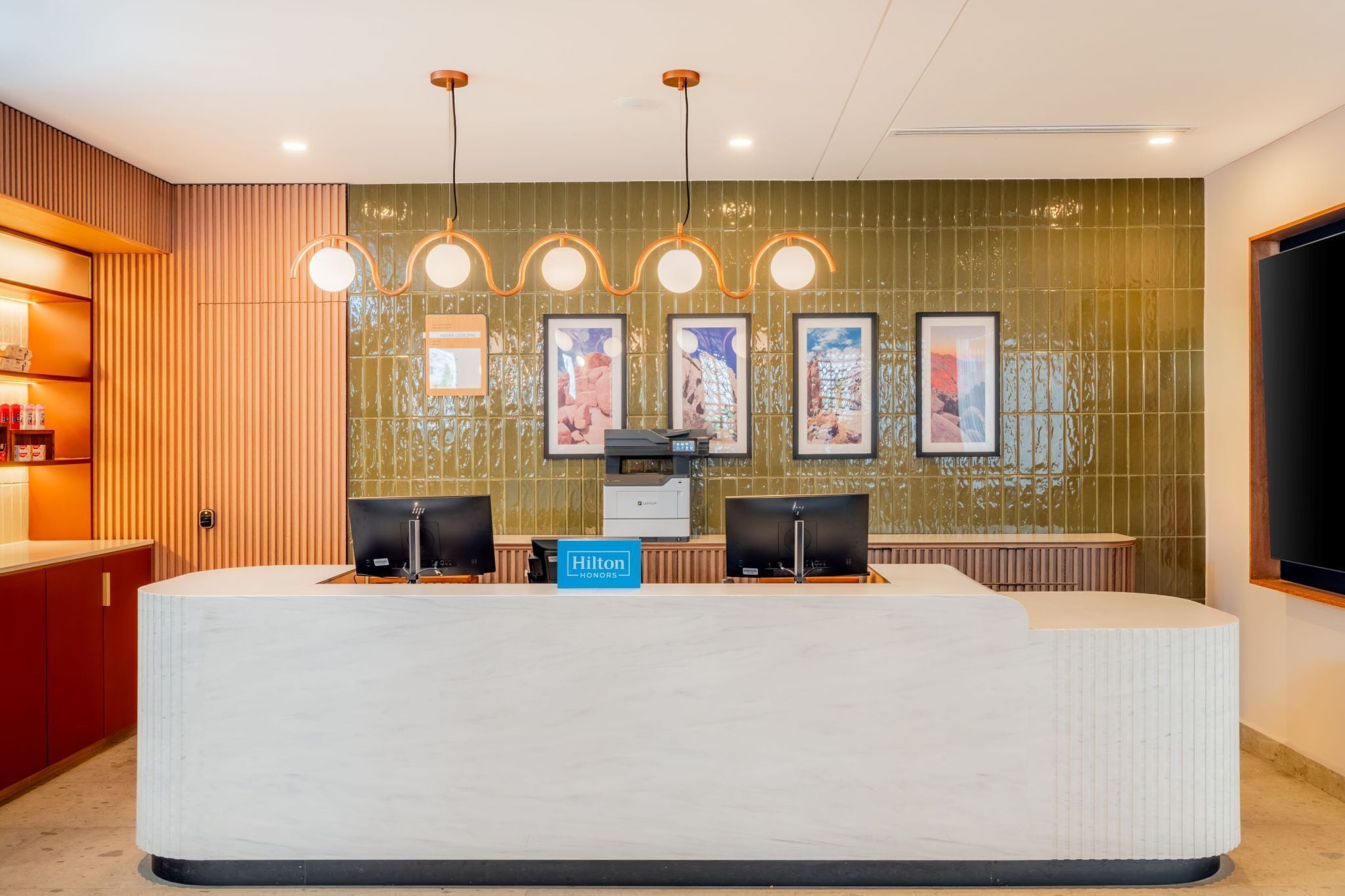 Een receptiebalie van een hotel met twee monitoren, een digitaal scherm en een bord waarop 'Hilton Honors' staat.