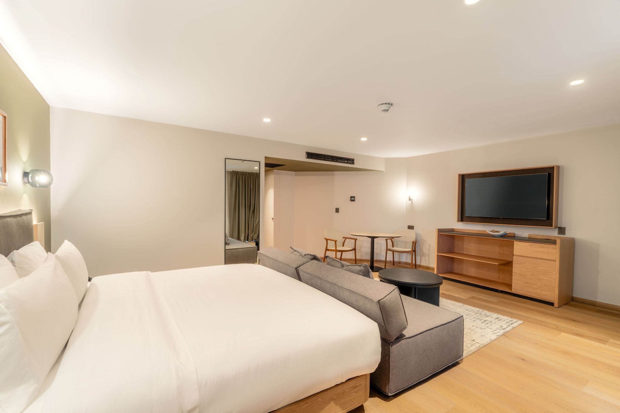 A modern hotel room with a large bed, a sofa, a dining table, and a TV.