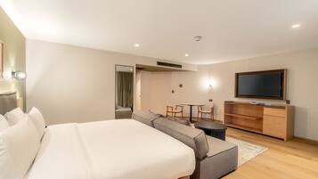 A modern hotel room with a large bed, a sofa, a dining table, and a TV.