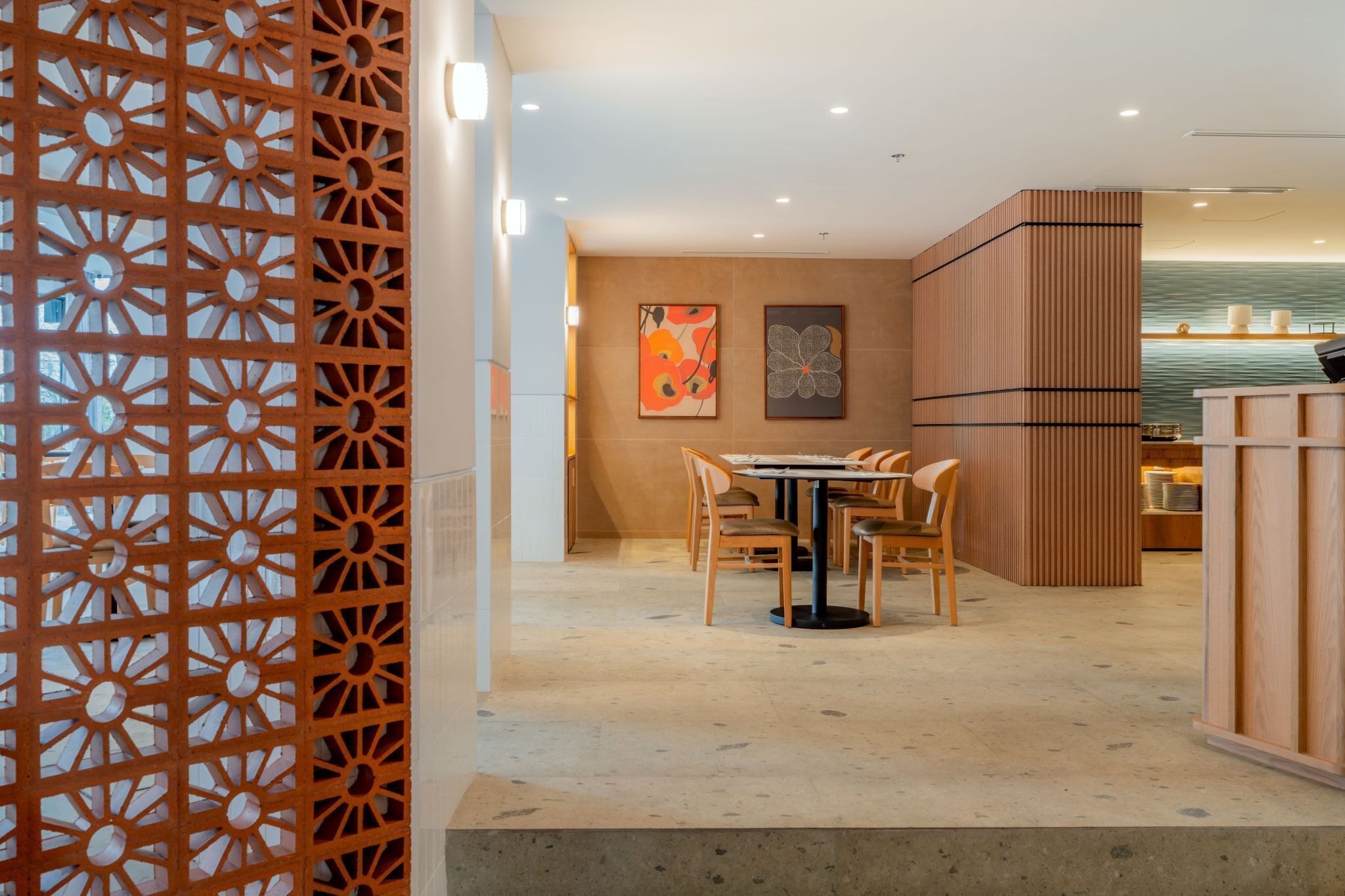 Un interior moderno con un comedor que incluye una mesa redonda y sillas, una pared decorativa con obras de arte, y un panel de madera con un diseño geométrico.