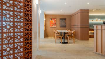 Un interior moderno con un comedor que incluye una mesa redonda y sillas, una pared decorativa con obras de arte, y un panel de madera con un diseño geométrico.