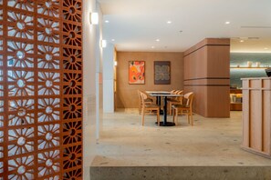 A modern interior with a dining area featuring a round table and chairs, a decorative wall with artwork, and a wooden partition with a geometric pattern.