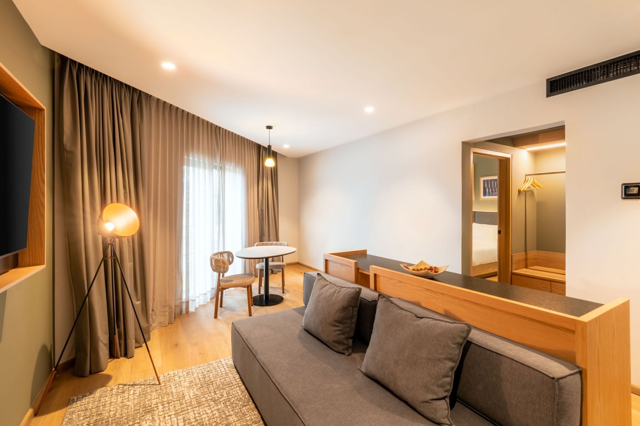 A modern hotel room with a sofa, a dining table, a chair, a lamp, and a large mirror.