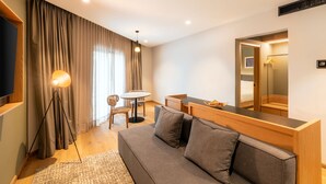 A modern hotel room with a sofa, a dining table, a chair, a lamp, and a large mirror. - Hilton Garden Inn Tijuana Airport (Tijuana)