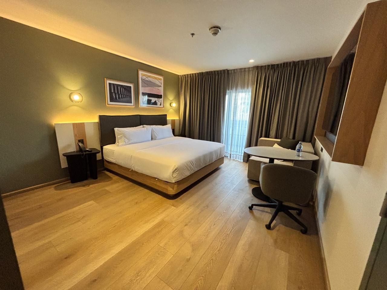 A hotel room with a bed, desk, chair, and a view of the outdoors.