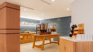 A modern cafe interior with a wooden counter, a seating area, and a wall-mounted coffee machine. - Hilton Garden Inn Tijuana Airport (Tijuana)