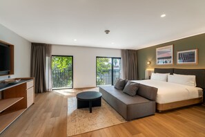 A modern hotel room with a bed, a sofa, a TV, and a balcony with curtains. - Hilton Garden Inn Tijuana Airport (Tijuana)