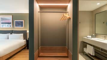 Una habitación de hotel con cama, zona de ducha y baño con espejo y toallero.
