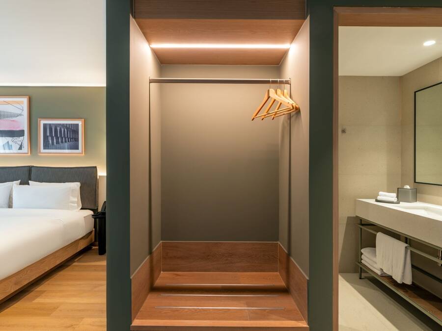 Una habitación de hotel con cama, zona de ducha y baño con espejo y toallero.