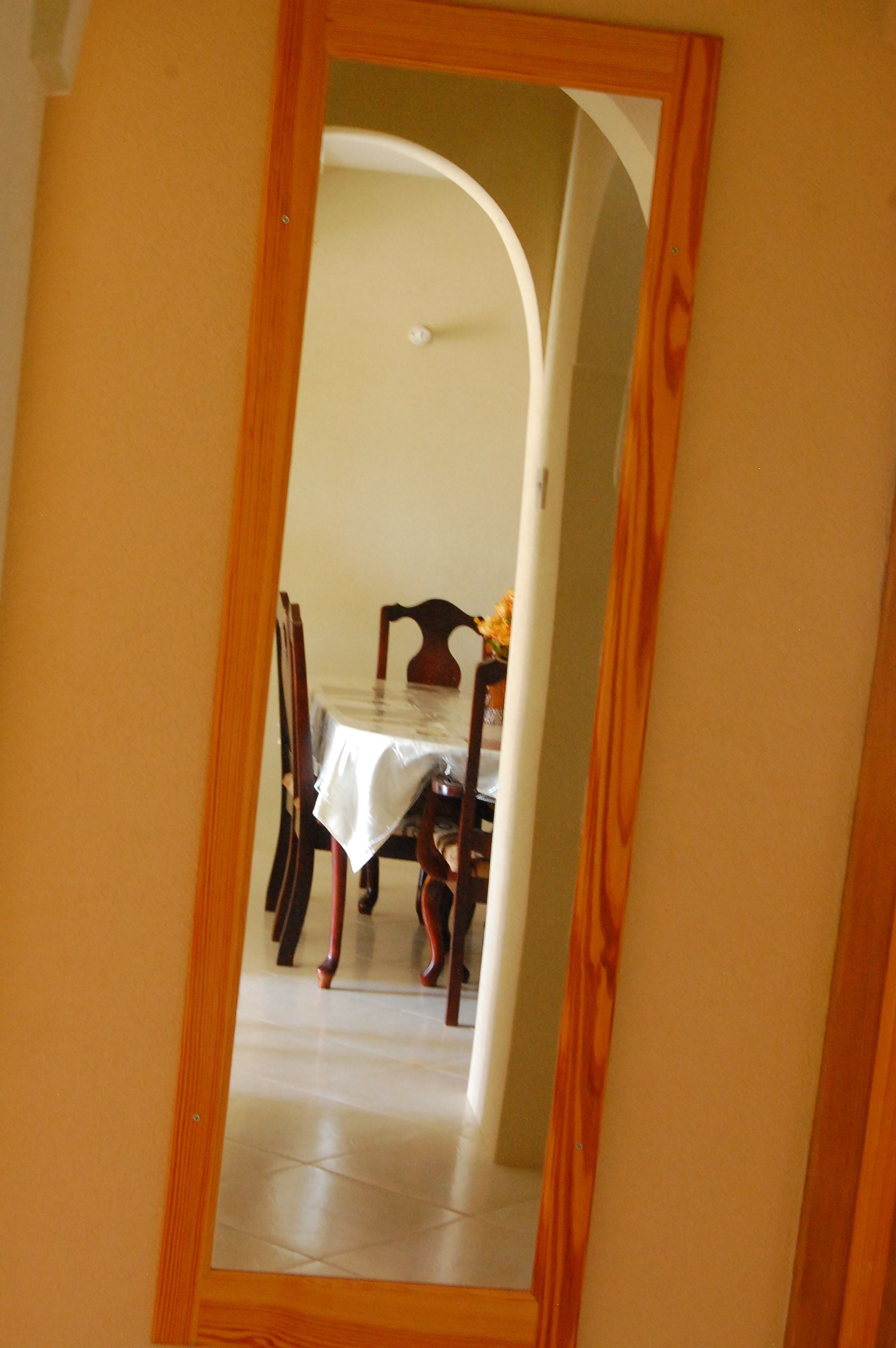 A mirror reflecting a dining area with a table, chairs, and a vase of flowers.