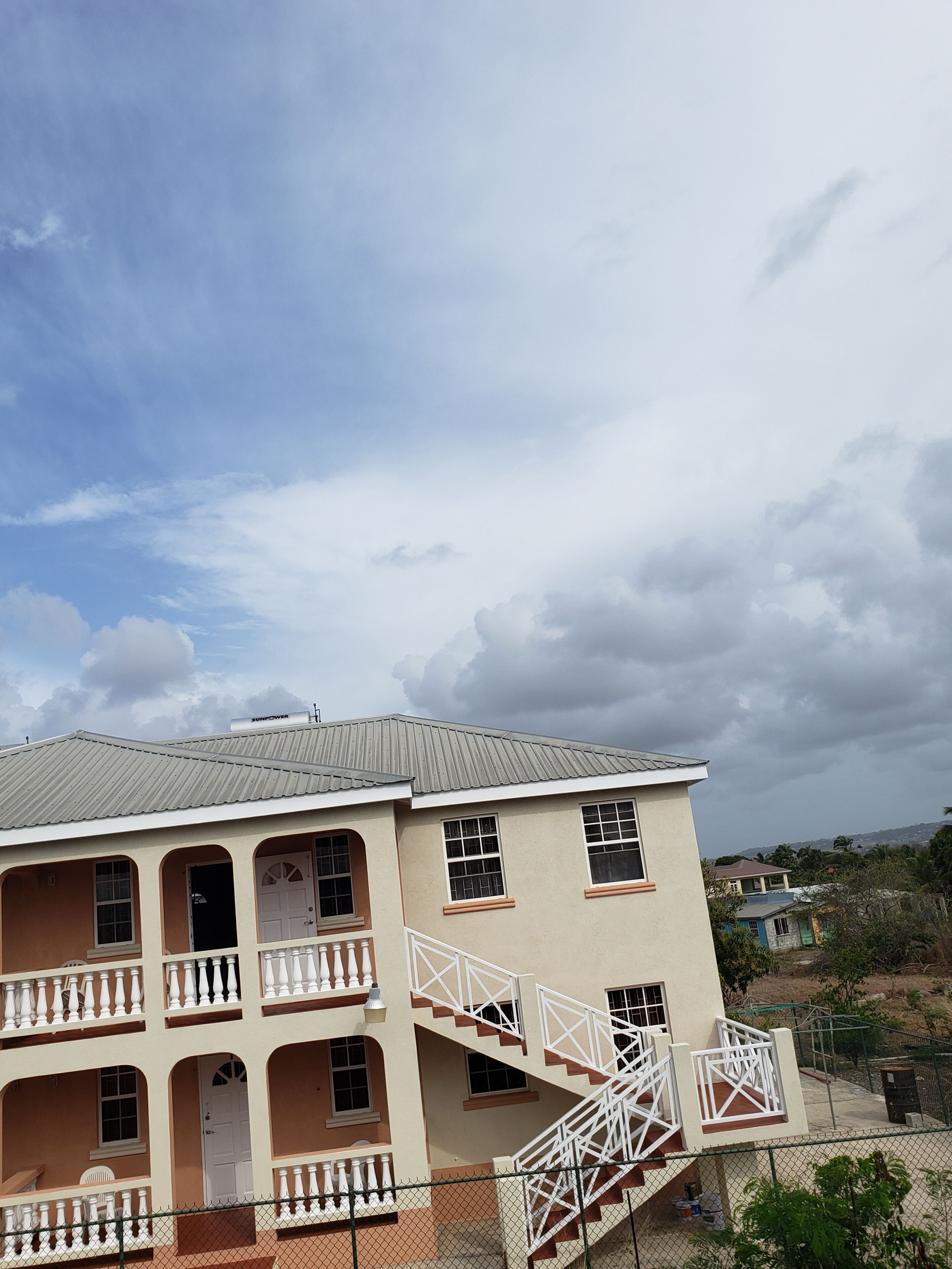 A two-story building with a balcony, a staircase, and a fenced yard.