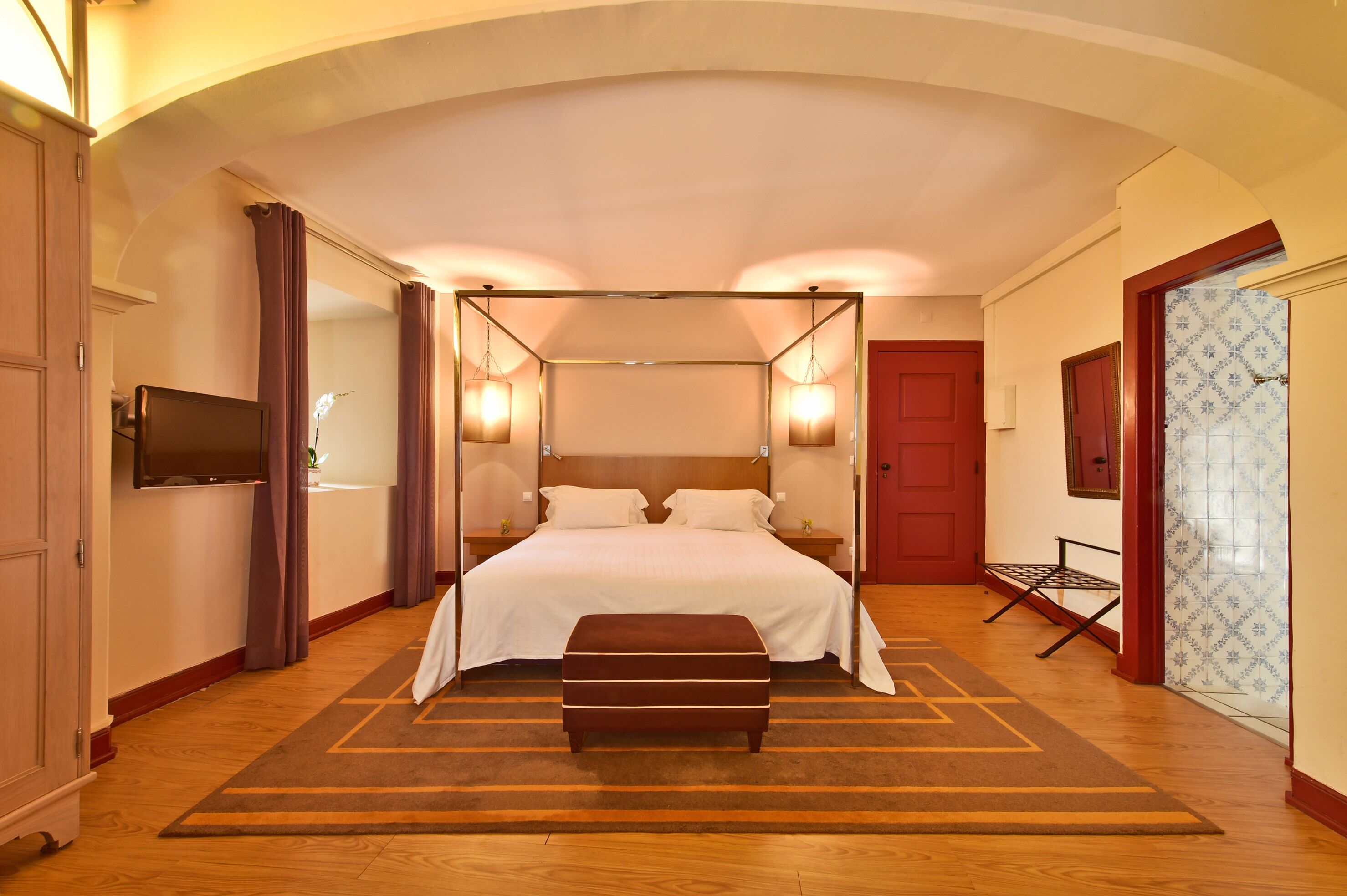 Ein Schlafzimmer mit Himmelsbett, Flachbildfernseher, Nachttisch und roter Tür.