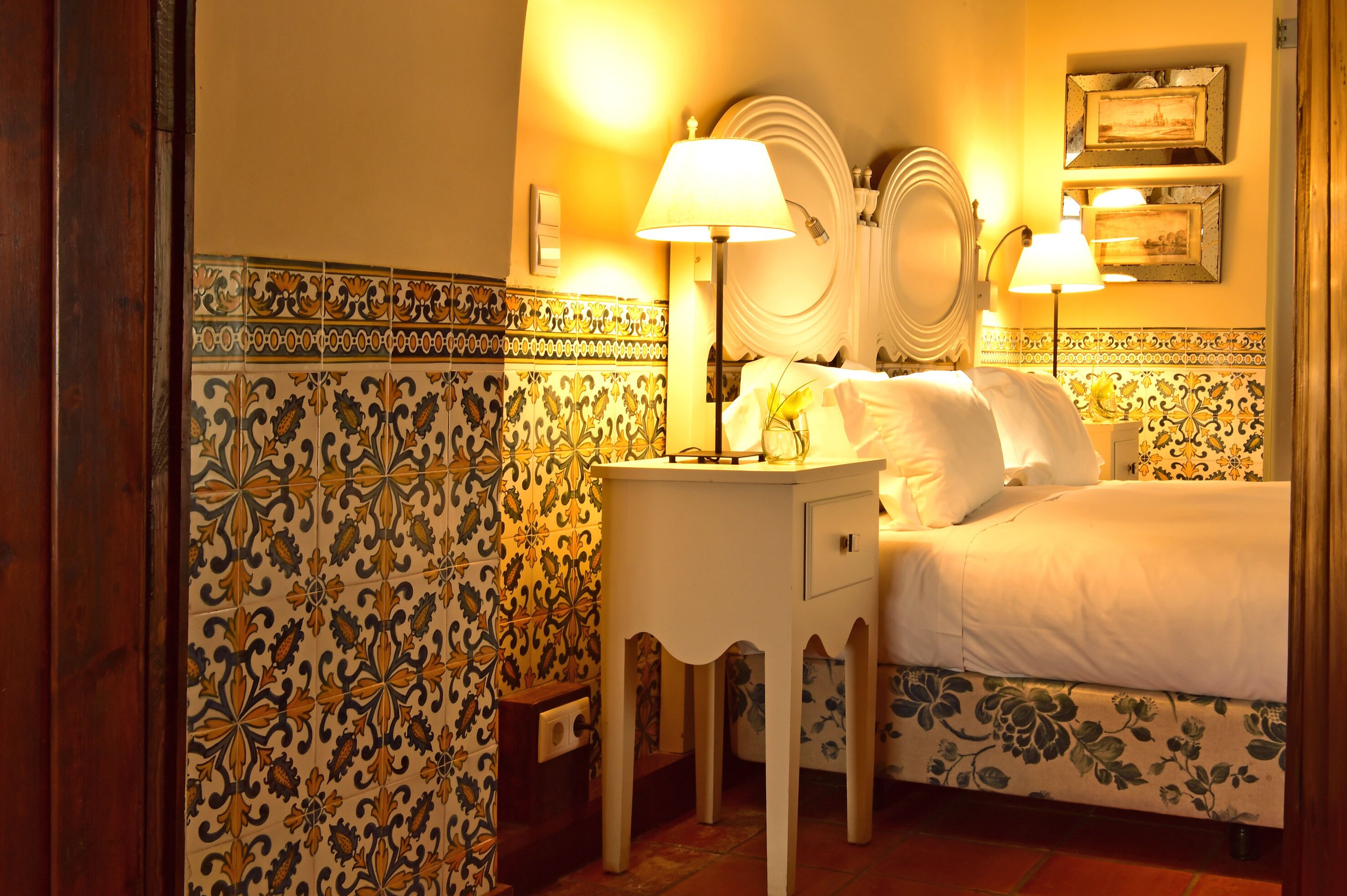 Ein Hotelzimmer mit einem Bett, zwei Nachttischlampen, einem kleinen Tisch und einer dekorativen Wand mit Kacheln.