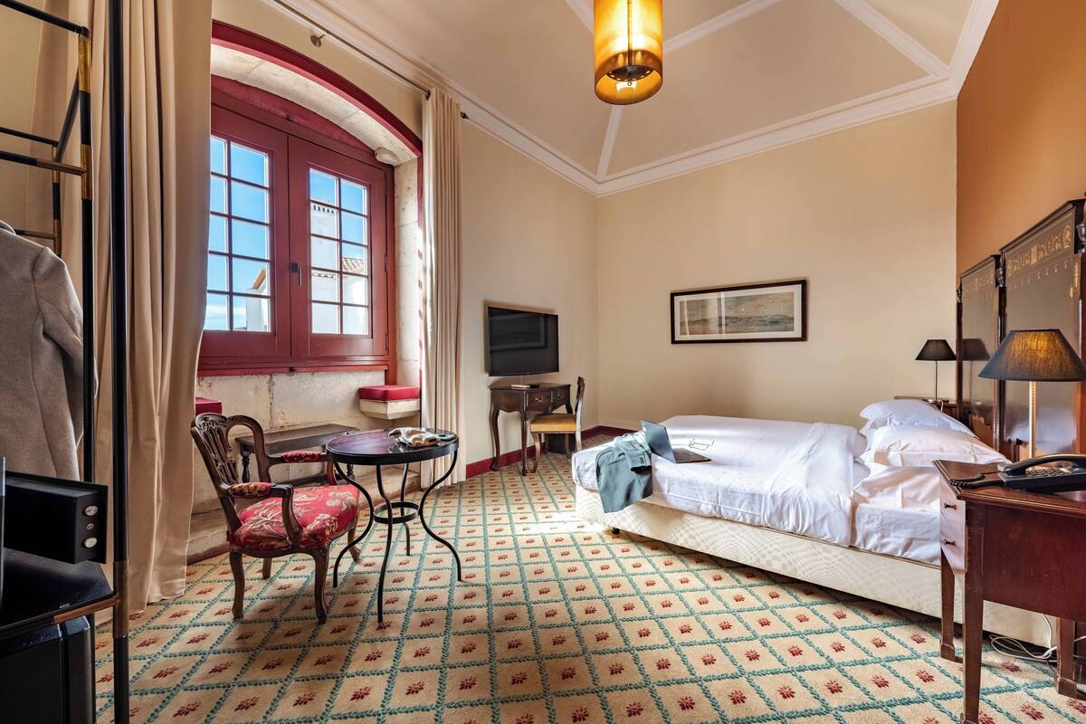 Ein Hotelzimmer mit Bett, Schreibtisch, Stuhl, Fernseher und einem Fenster mit Vorhängen.