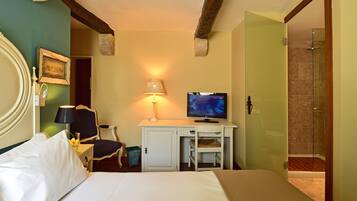 Habitación de hotel con cama, escritorio con televisor, una silla, lámpara y zona de ducha.