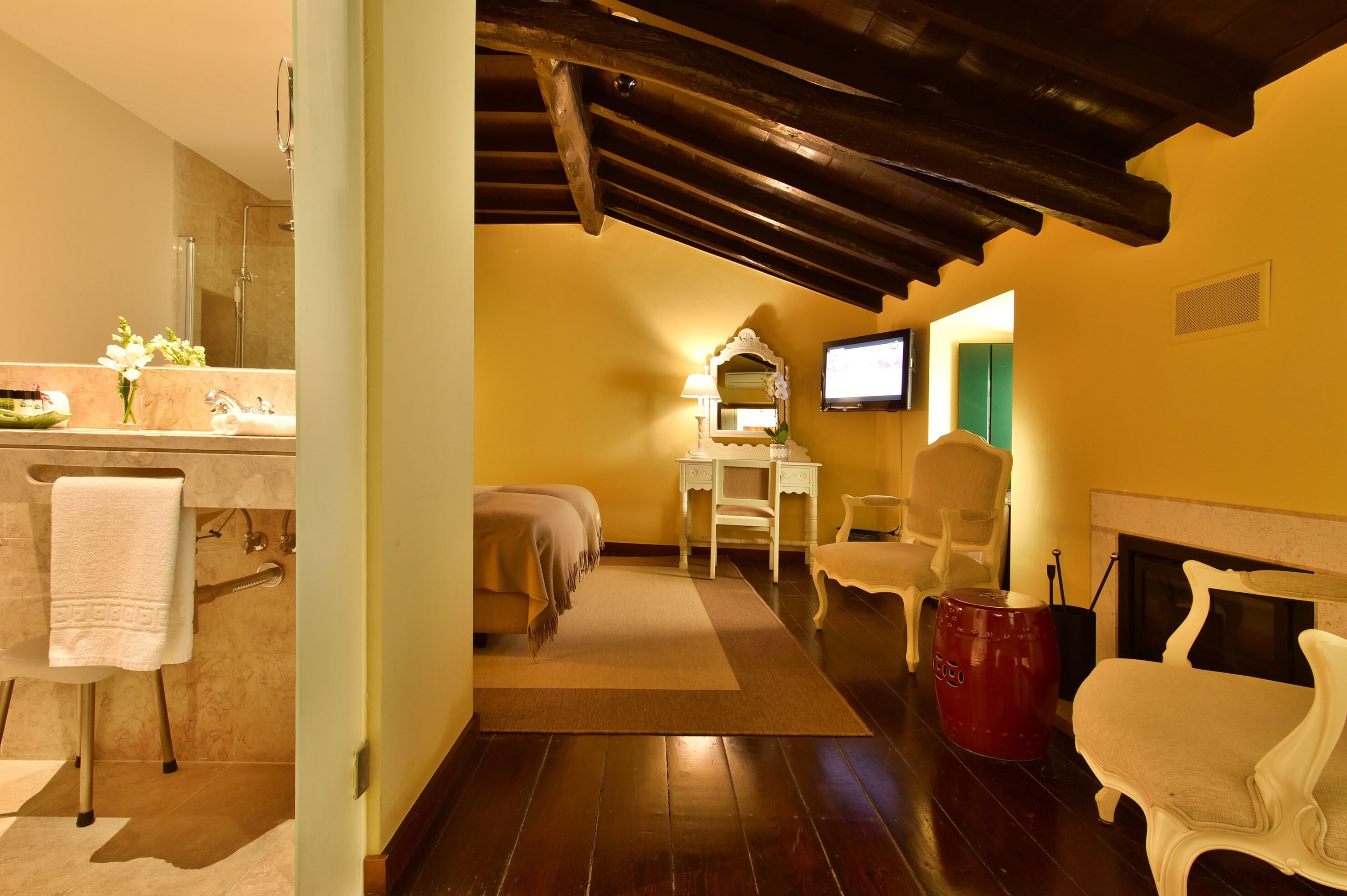 A hotel room with a wooden ceiling, a fireplace, a TV, a desk, and a bed.