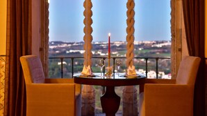 A table set for two with a candle, glasses, and a small vase, overlooking a scenic view through a window with ornate balustrades. - Pousada Castelo de Óbidos - Historic Hotel (Obidos)