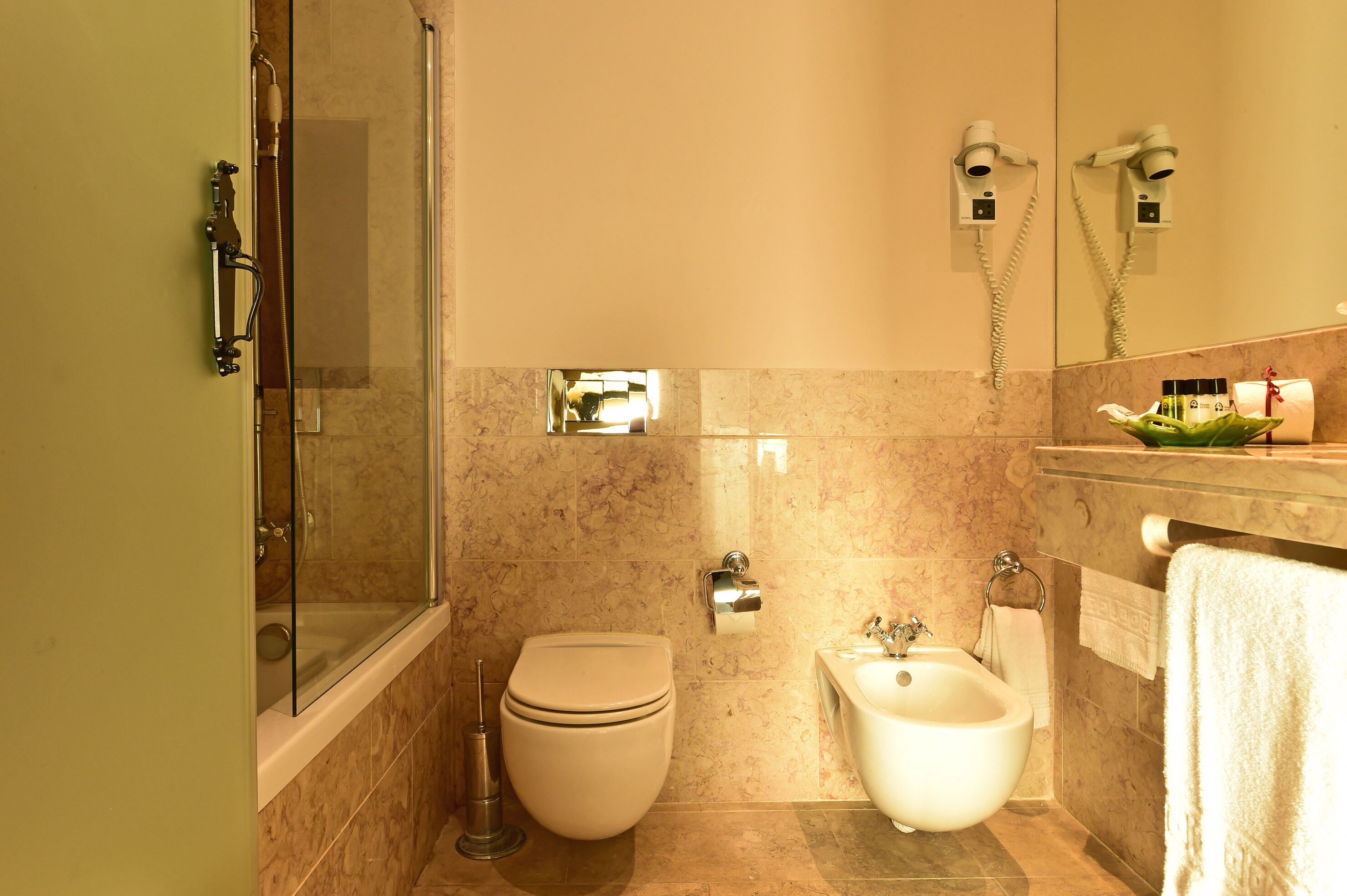 Un baño con inodoro, bidé y ducha con mampara de vidrio.