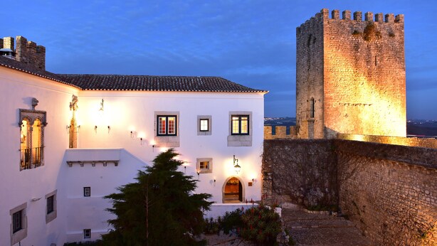 A historic building with a stone tower and a white facade with multiple windows and a door. - Pousada Castelo de Óbidos - Historic Hotel (Obidos)
