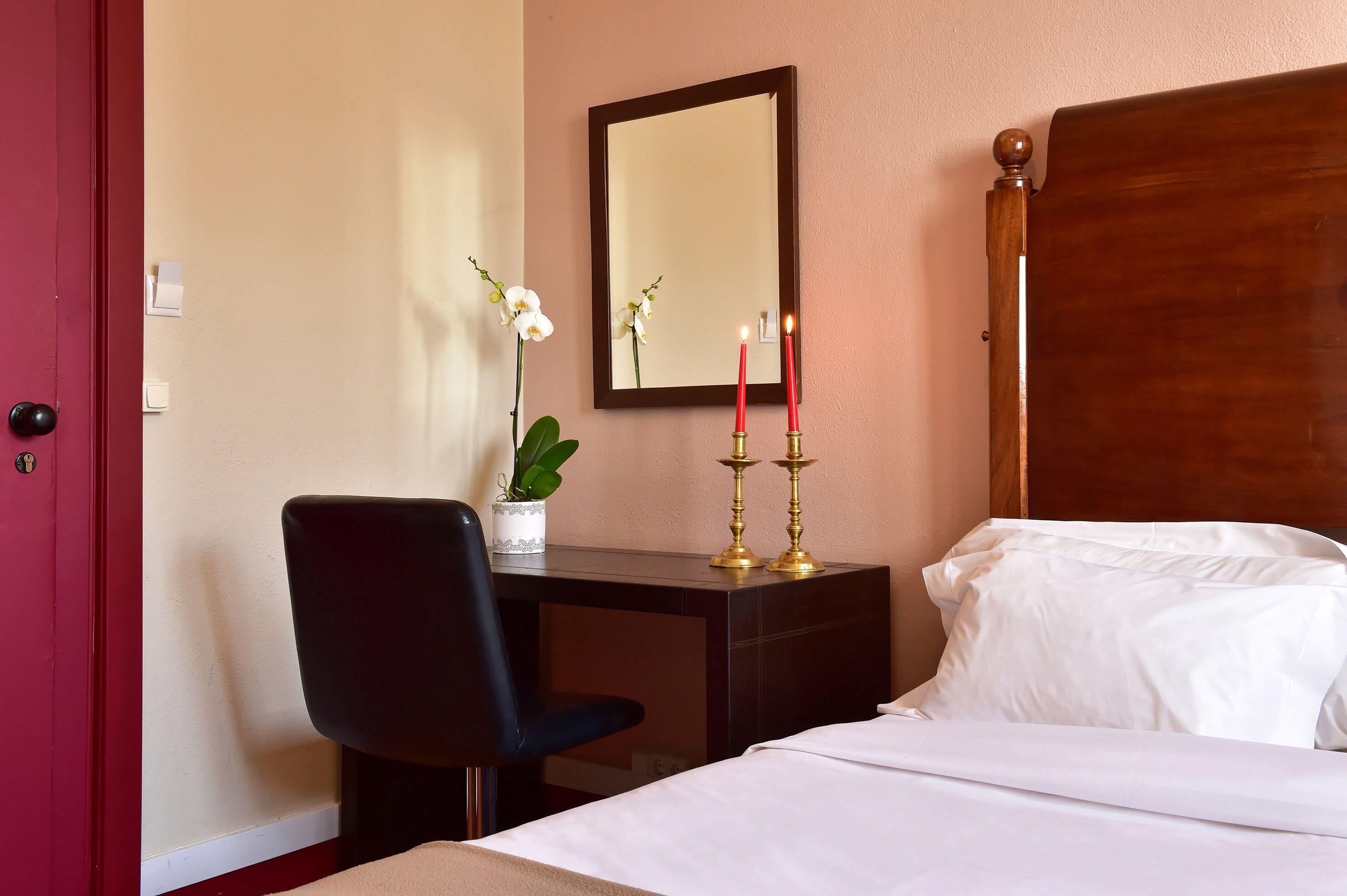 Habitación de hotel con cama, escritorio con silla, florero con flores y dos velas.