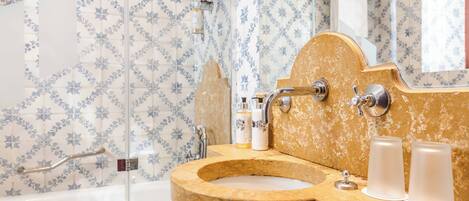 A bathroom with a marble sink, a bathtub, and a shower. There are toiletries on the sink and a towel rack above the bathtub.