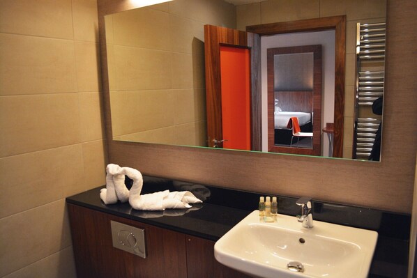 A bathroom with a black countertop, a white sink, and a mirror reflecting a door and a towel rack.
