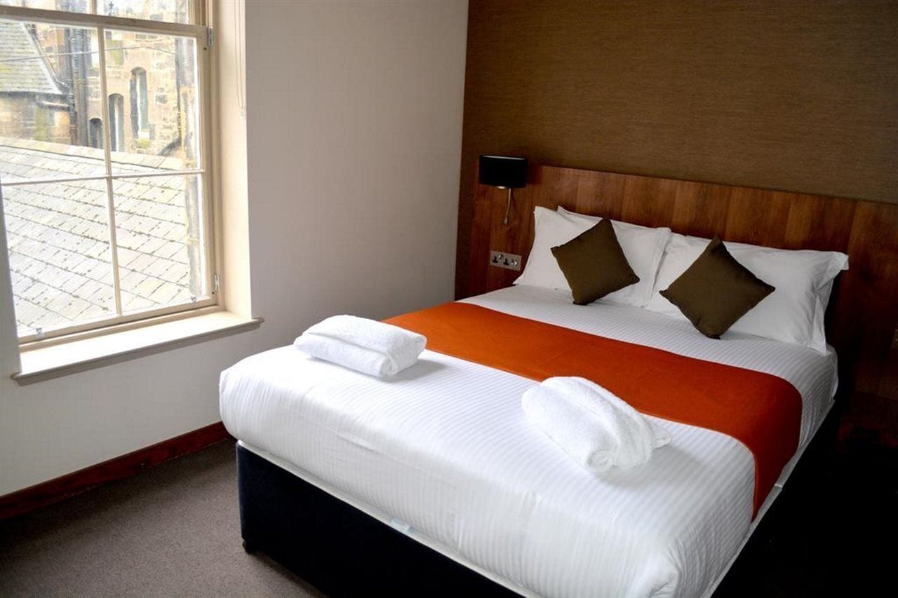 Une chambre d’hôtel avec un grand lit, une fenêtre donnant sur des immeubles et une table de chevet avec une lampe.