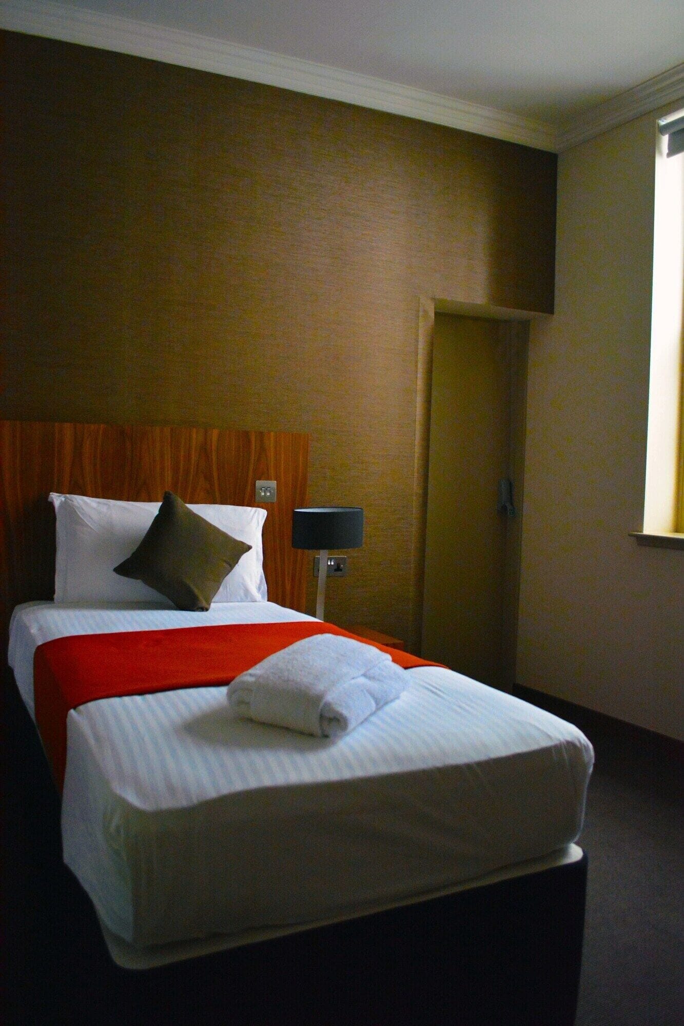 A hotel room with a bed, a nightstand, a lamp, and a door.