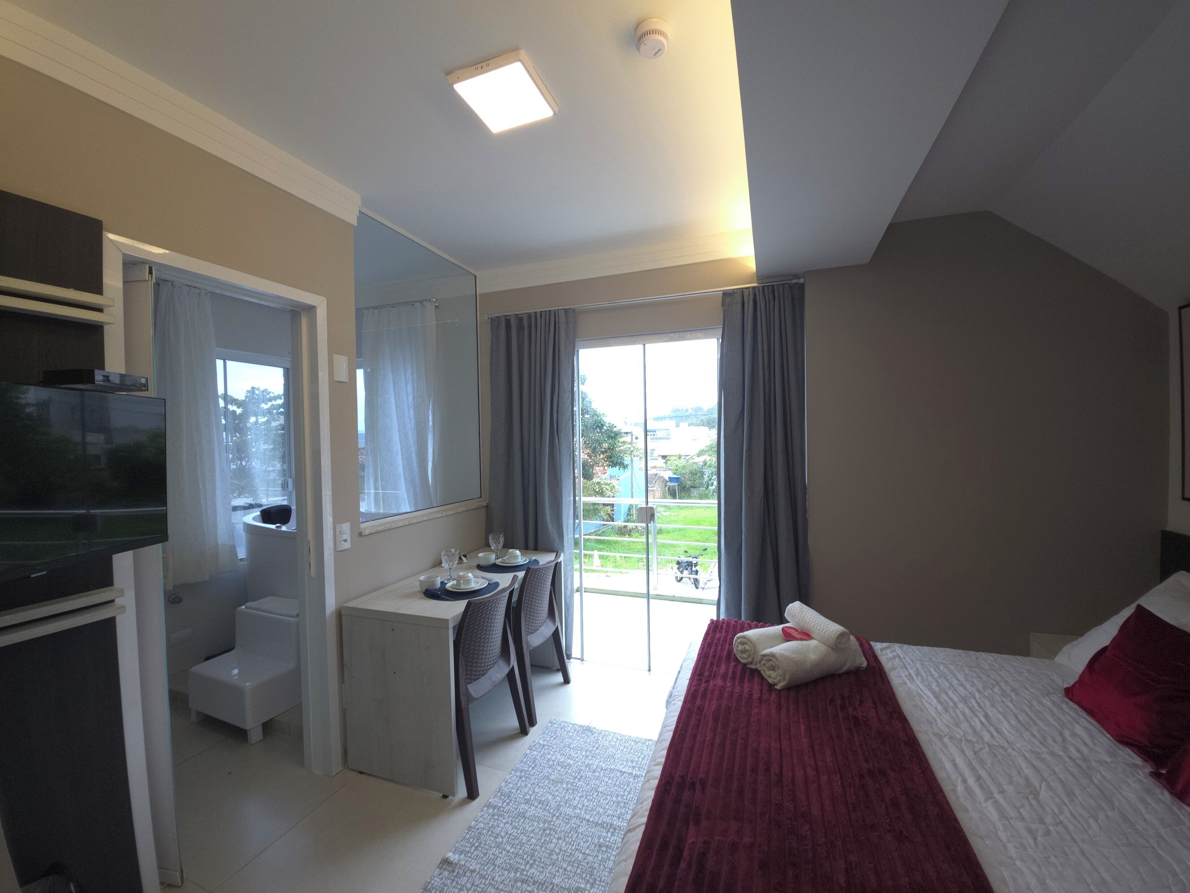 A hotel room with a bed, a desk, a television, and a view of the outdoors.